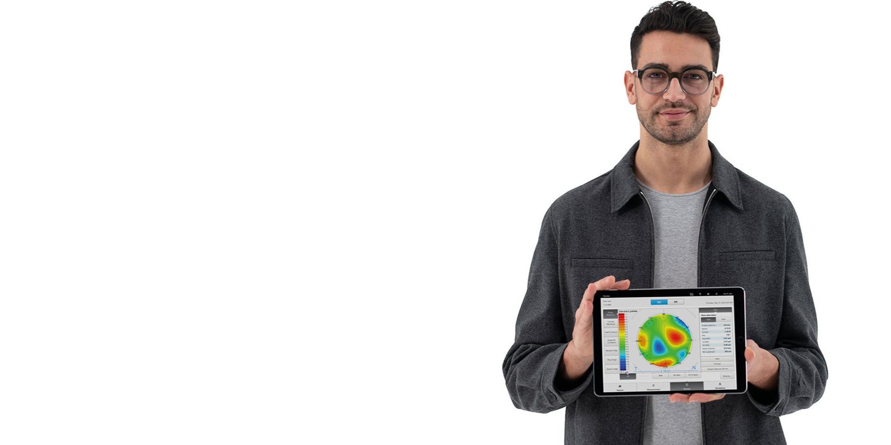 Молодий чоловік у лінзах ZEISS дивиться в камеру, тримаючи iPad із попередньою інформацією для точної об’єктивної рефракції.