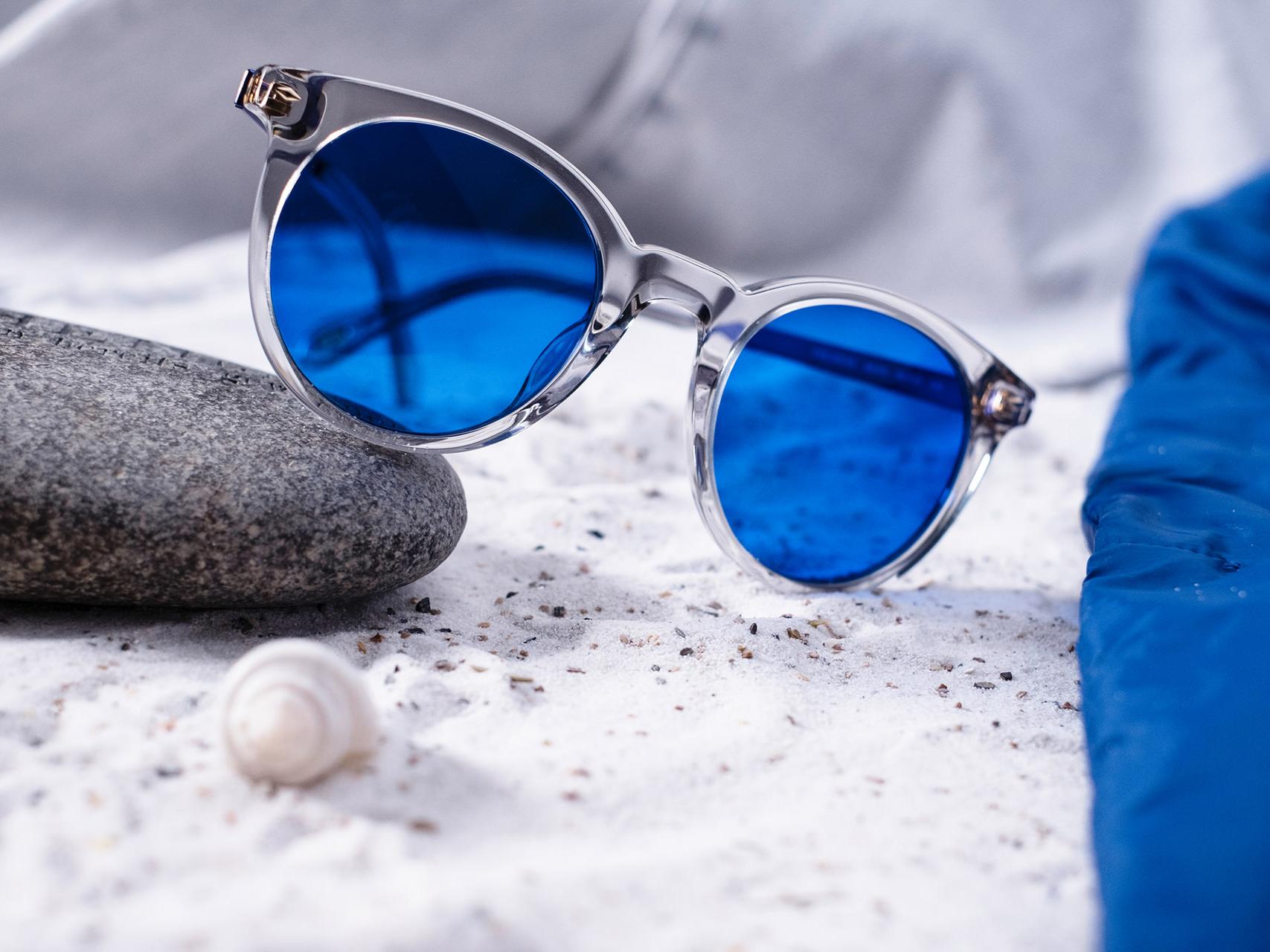 Зображення сонцезахисних окулярів із синім тонуванням, що наполовину лежать на камені