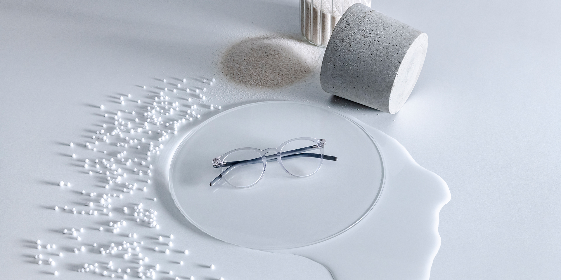 Лінзи ZEISS із покриттям DuraVision® на скляній підставці в оточенні води, піску, гранул і каменю.