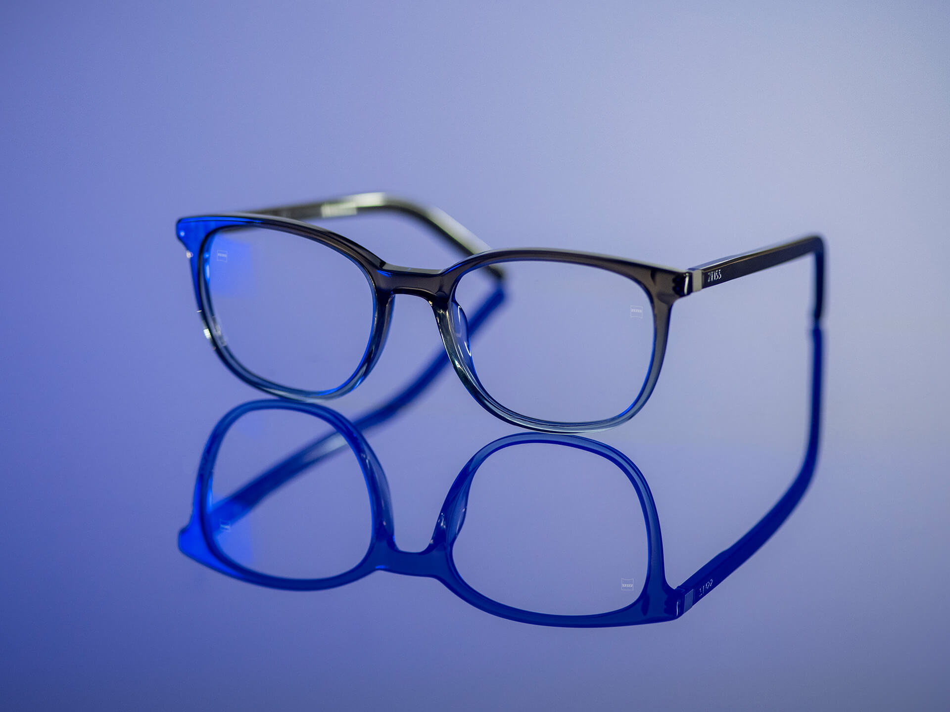 В синюватому світлі лежать окуляри з лінзами ZEISS, виготовленими з матеріалу BlueGuard. На лінзах видимі тільки дуже незначні синюваті відблиски.