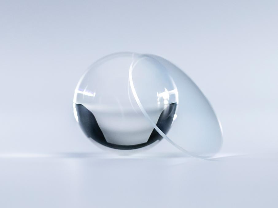 Лінза з покриттям ZEISS Platinum кришталево-прозора й не має відблисків порівняно зі скляною кулькою, що лежить поруч із нею.