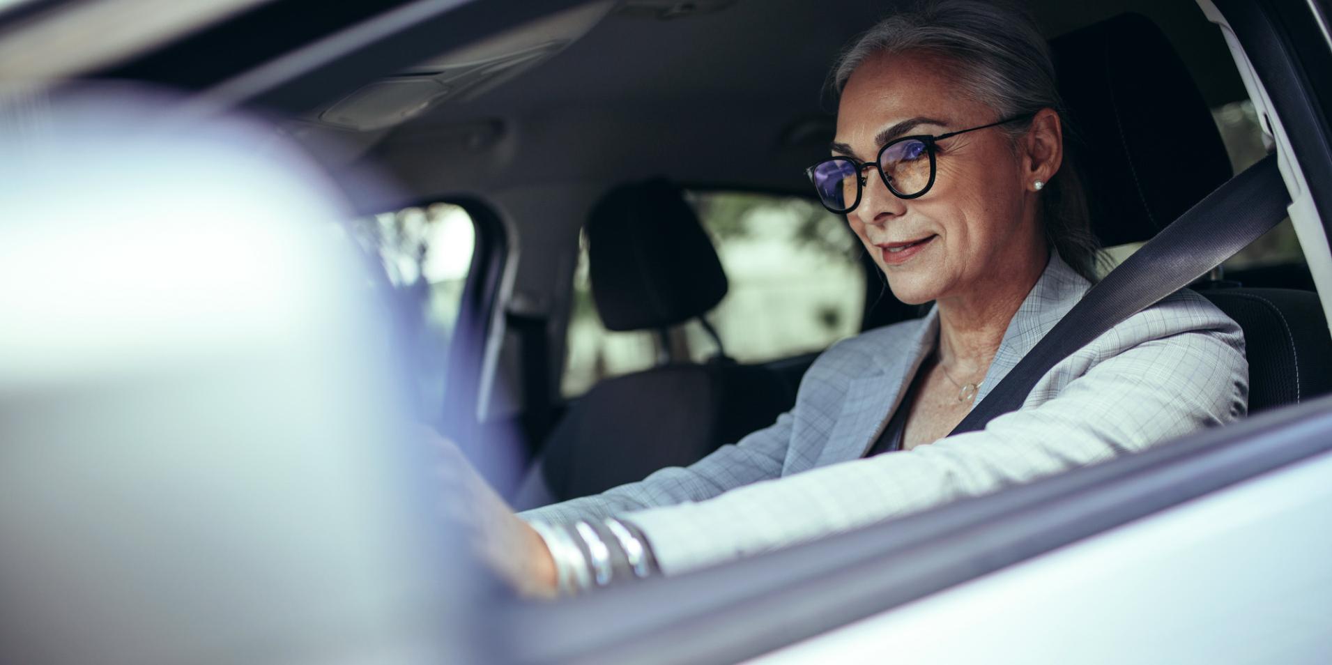 Літня жінка в окулярах із лінзами ZEISS DriveSafe за кермом авто.
