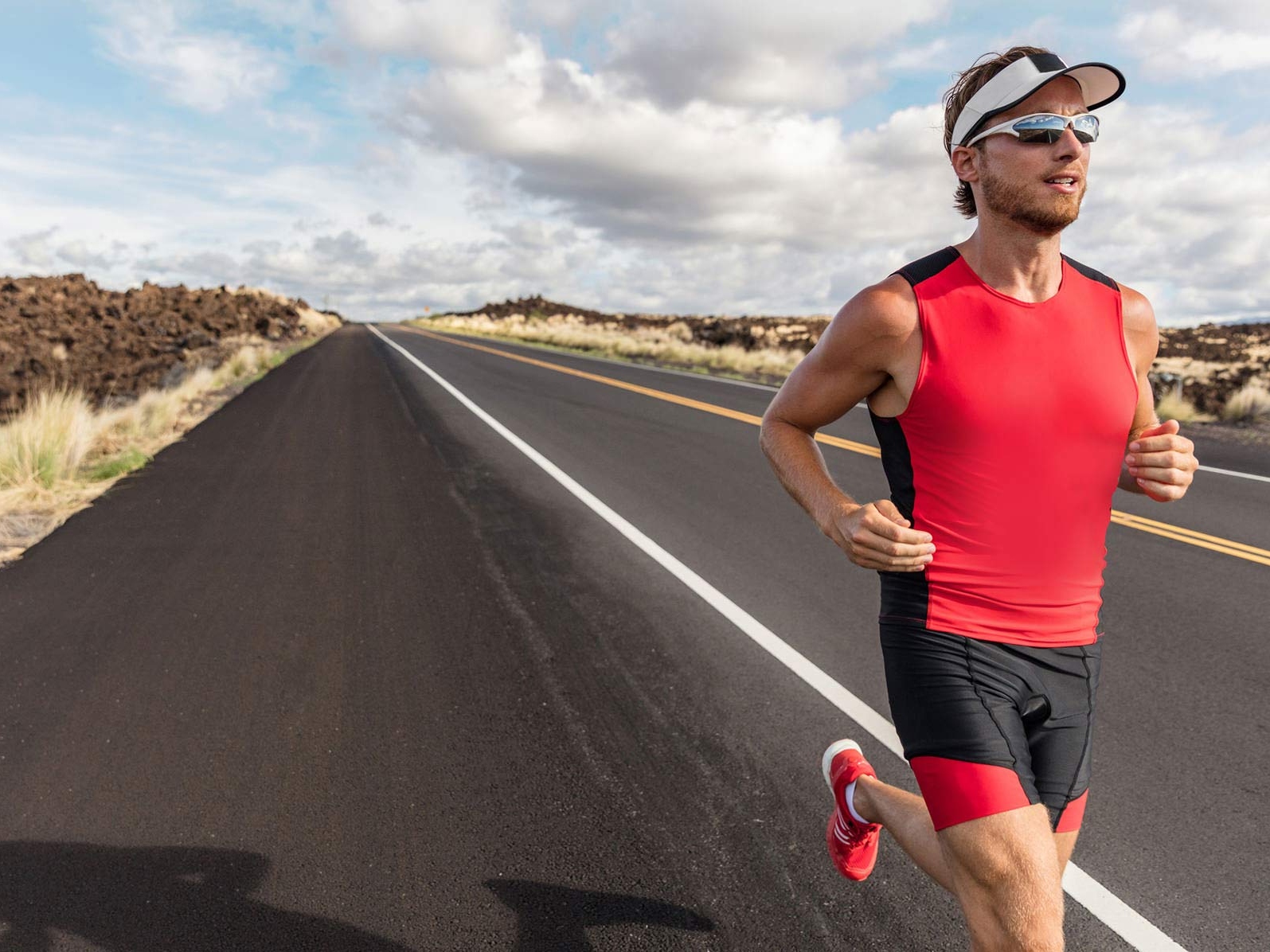 Зображення чоловіка в спортивному одязі та спортивних окулярах, який біжить дорогою. 